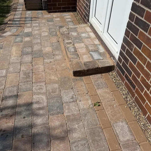 Block paved side path in buff and brown tones running past a back door, with a timber step