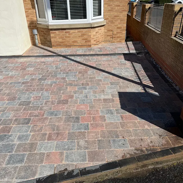 Brindle block paving driveway running alongside a brick garden wall with railings