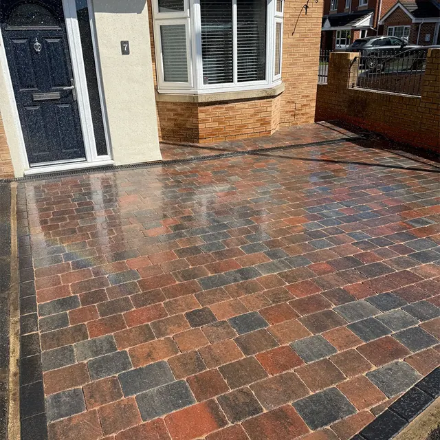 Brindle block paving driveway with a charcoal border in front of a bay-window house with a black front door