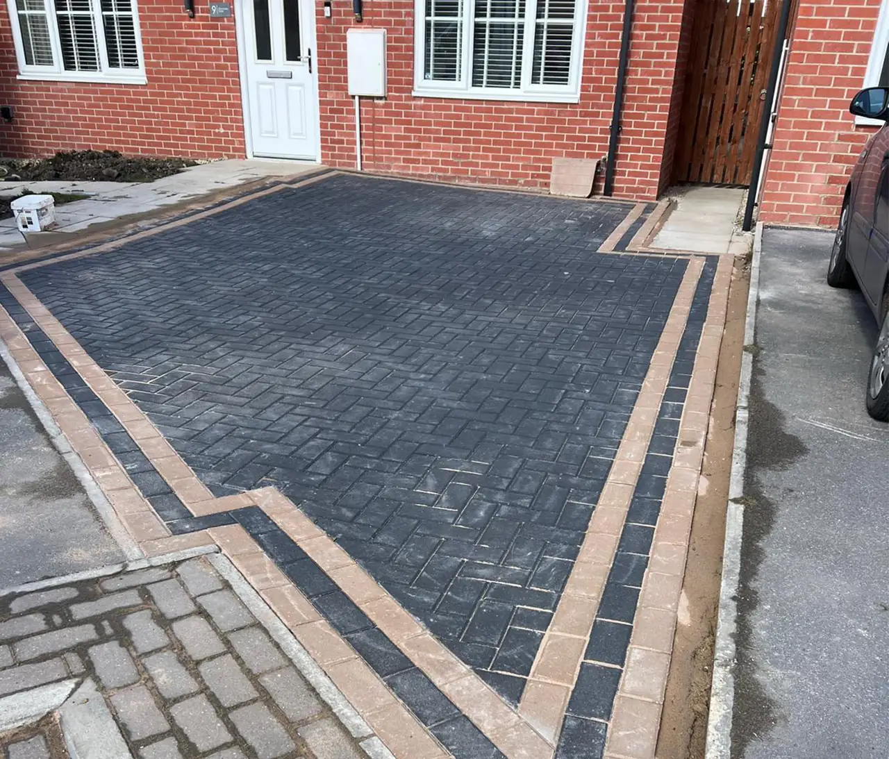 Charcoal block paving driveway with a stepped buff border, laid in front of a red-brick semi
