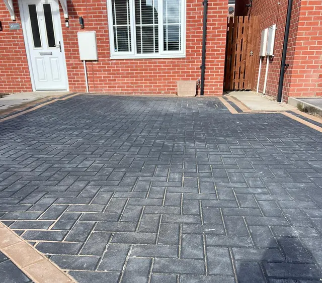 Charcoal herringbone block paving driveway with a double buff border, laid up to the front door of a red-brick house