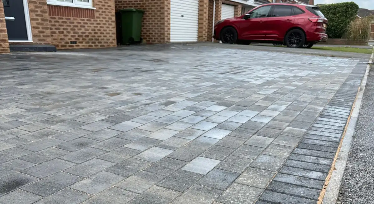 Grey block paving driveway in mixed tones with a charcoal edge, outside a brick house and garage