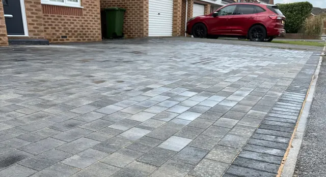 Grey mixed-tone block paving driveway with a charcoal edge, outside a house and garage