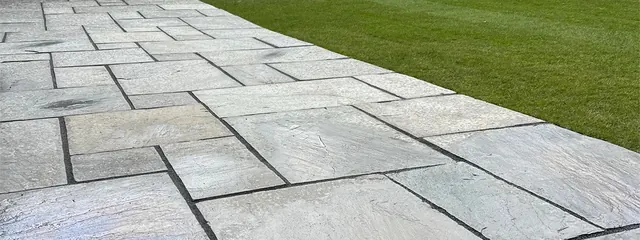 Grey sandstone paving laid in random sizes, running alongside a striped lawn
