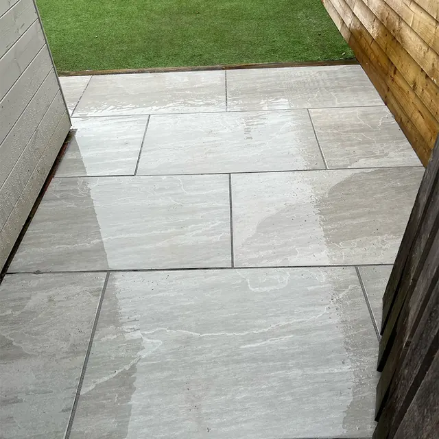 Large grey paving slabs laid as a side path between a timber fence and a building, leading to a lawn