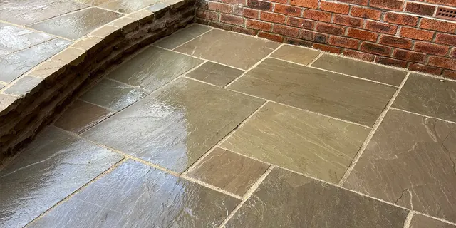 Wet Indian sandstone patio with a raised stone retaining wall and a red brick boundary wall