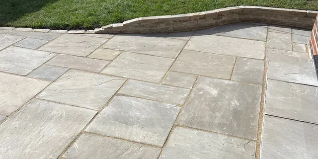 Newly laid sandstone patio behind a house, with a curved raised stone edge between the patio and the lawn